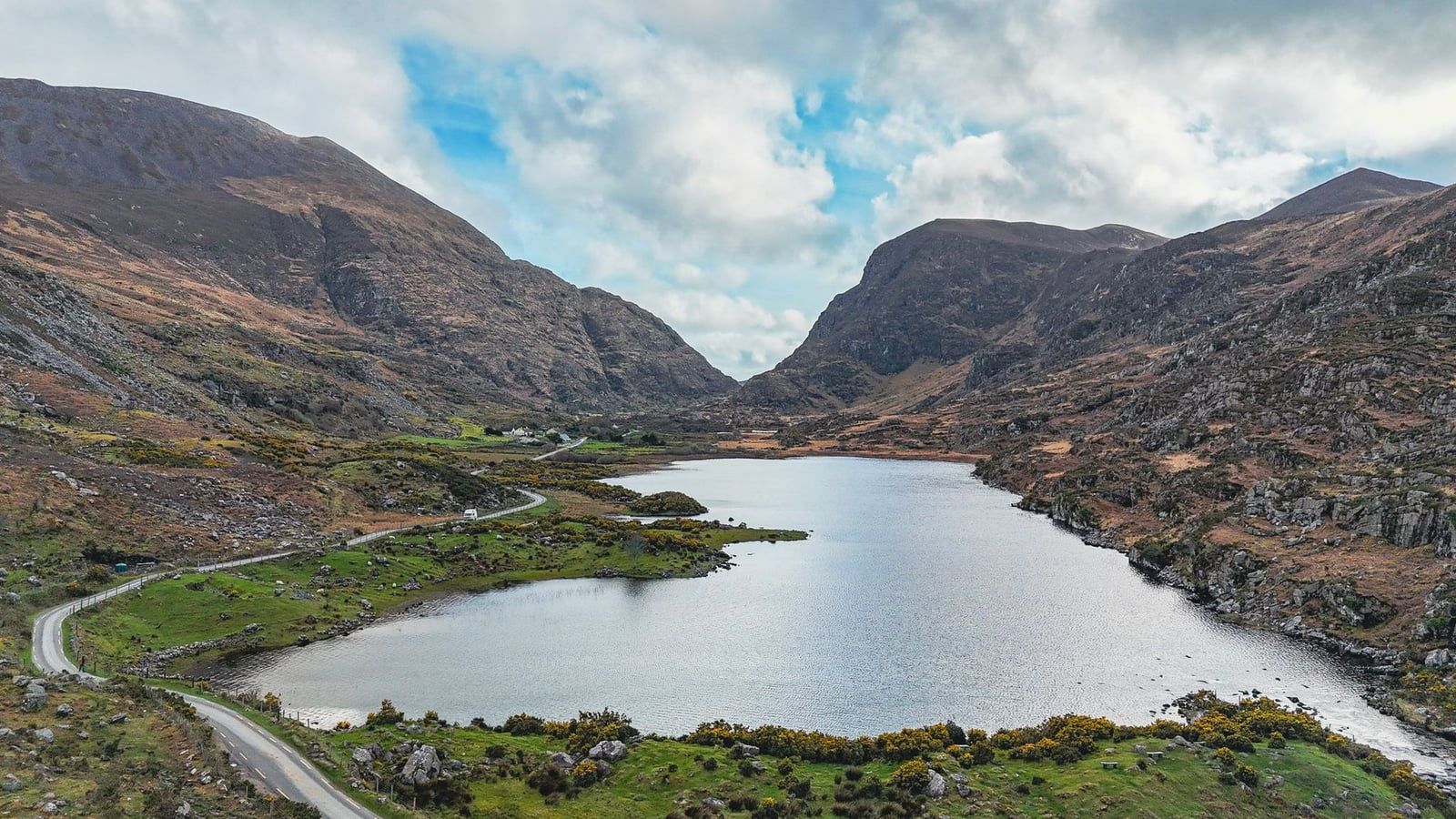 A winding road runs beside a lake nestled between rugged mountains in the Gap of Dunloe near Killarney National Park.