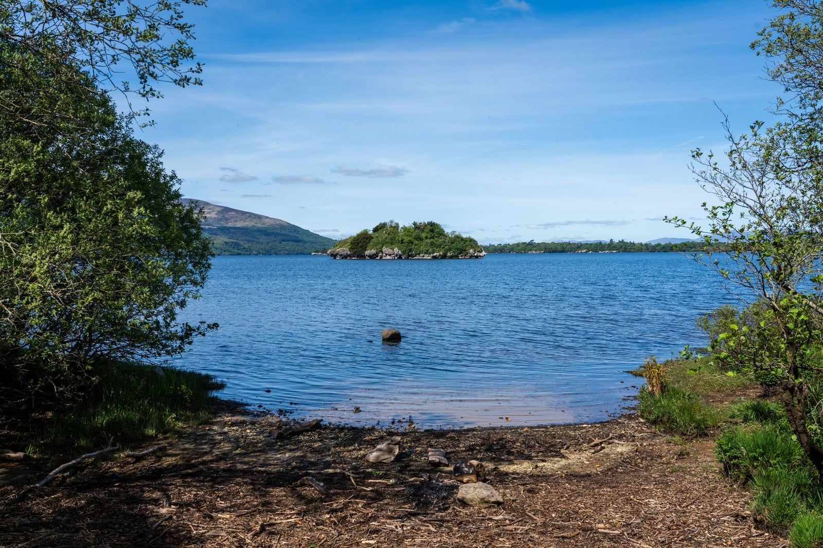A small wooded island sits in the blue waters of Lough Leane, framed by trees and distant hills in Killarney National Park.