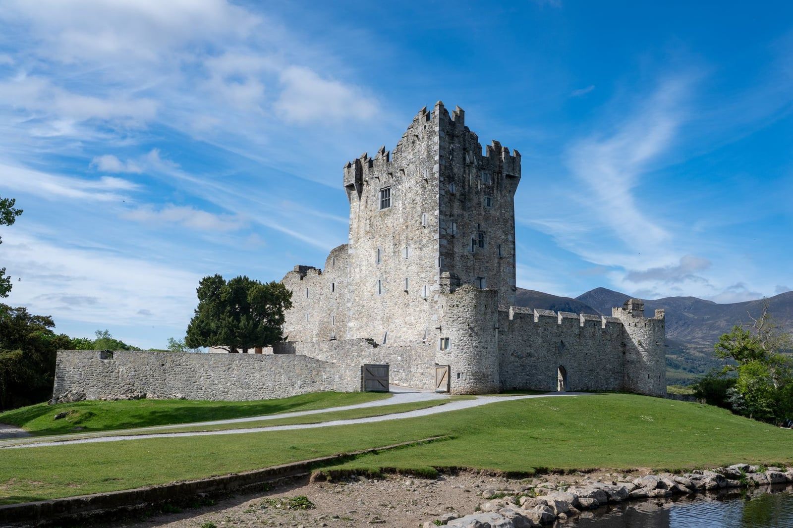 The stone tower house and surrounding bawn walls of Ross Castle stand on a grassy knoll in Killarney National Park.